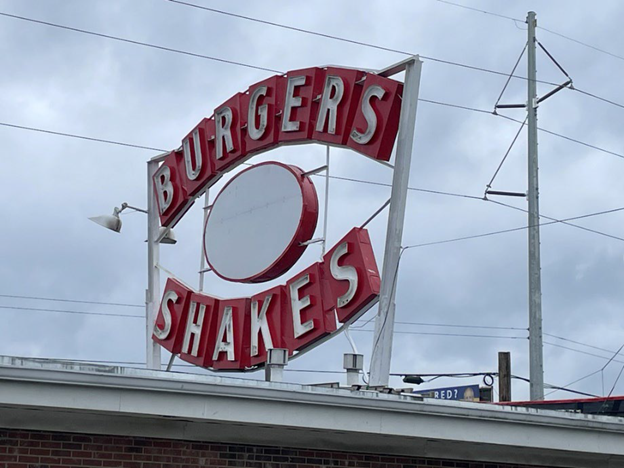 Modern day photo of historic burgers shakes sign atop a red roofed building